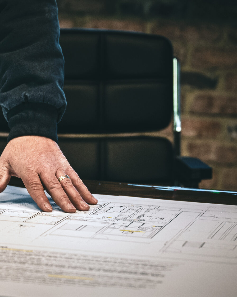 A hand resting on a set of construction drawings spread across a conference table